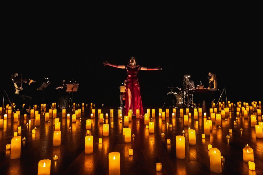 stage with heaps of candles and singer with outstretched arms supported by string quartet