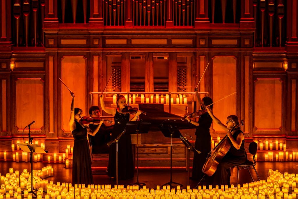 string quartet on stage with pianist surrounded by candles