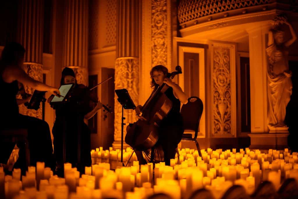 cellist in a string quartet performing surrounded by candles