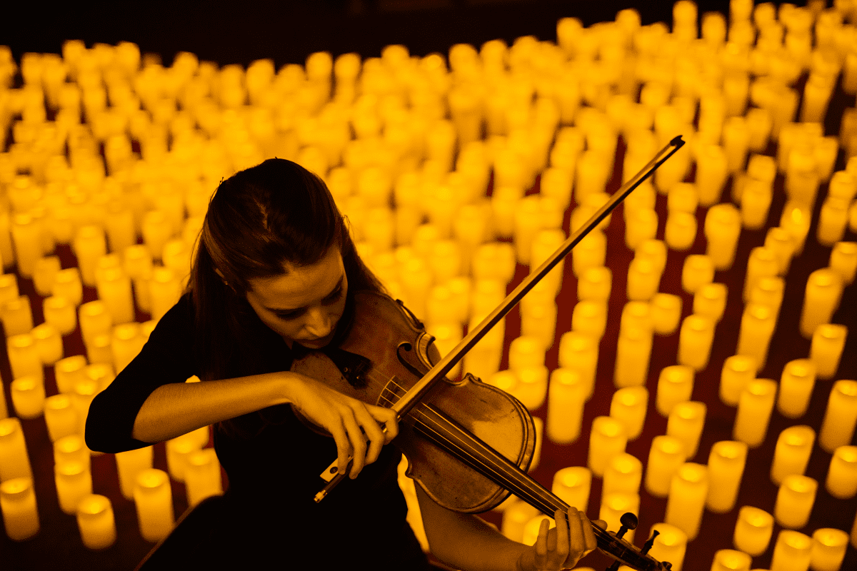 A woman playing the violin with a sea of candles behind her.