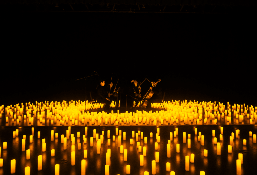 A string quartet performing on a stage surrounded by hundreds of candles.